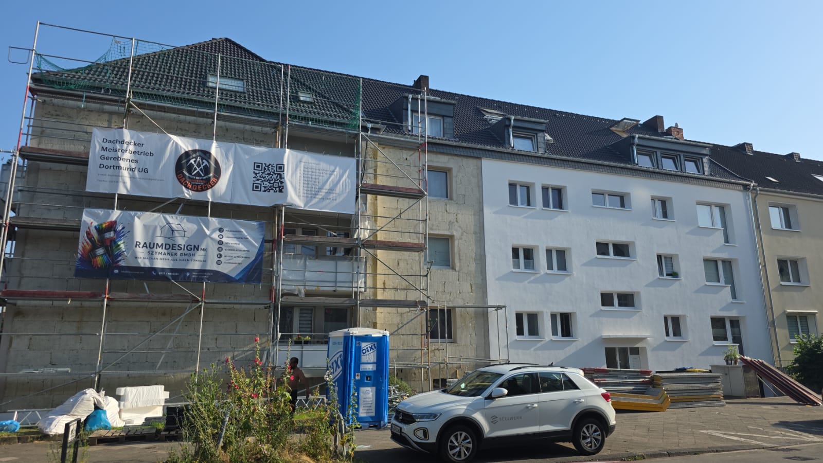 Mehrfamilienhaus mit neuem Dach und Gerüst mit Firmenbanner